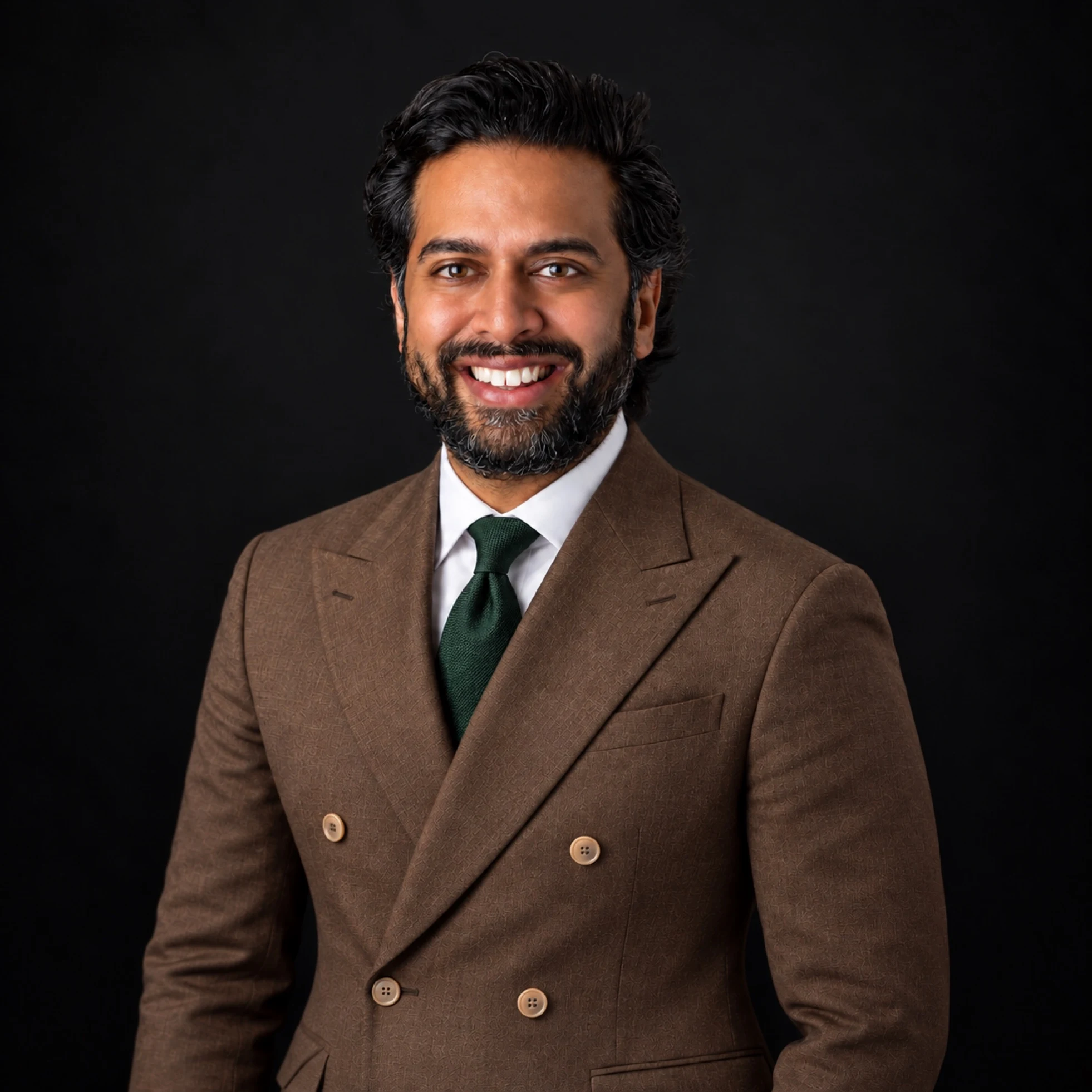 Portrait of Ricky K. Patel in a taupe double-breasted suit, white shirt, and dark hunter green tie against a dark studio background